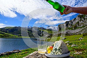 Pouring in glass of natural Asturian cider made fromÂ fermented apples, Asturian cabrales cow blue cheese with view on Covadonga
